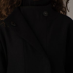 May include: A black mock neck coat with a single button closure. The coat has a long, flowing silhouette and a textured fabric.