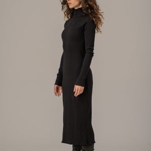 Puede incluir: Un vestido negro de punto de canal&eacute; con cuello alto y mangas largas, de largo midi. El vestido se lleva con botas negras de combate.