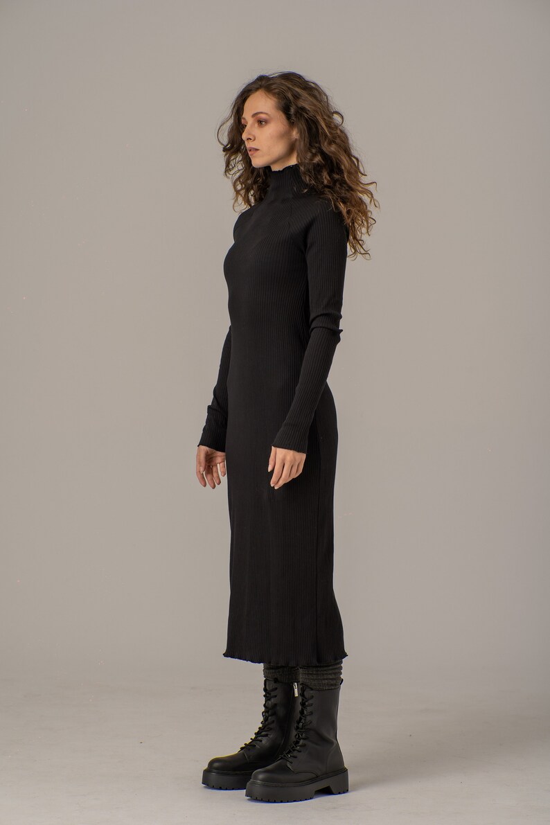 Puede incluir: Un vestido negro de punto de canal&eacute; con cuello alto y mangas largas, de largo midi. El vestido se lleva con botas negras de combate.
