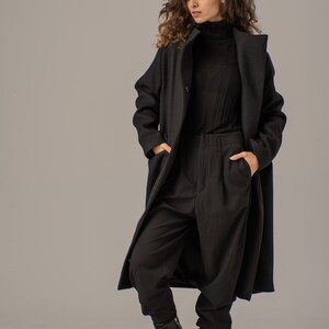May include: A woman wearing a black long-sleeved turtleneck shirt, black pants, and a black long coat. She is wearing black lace-up boots.