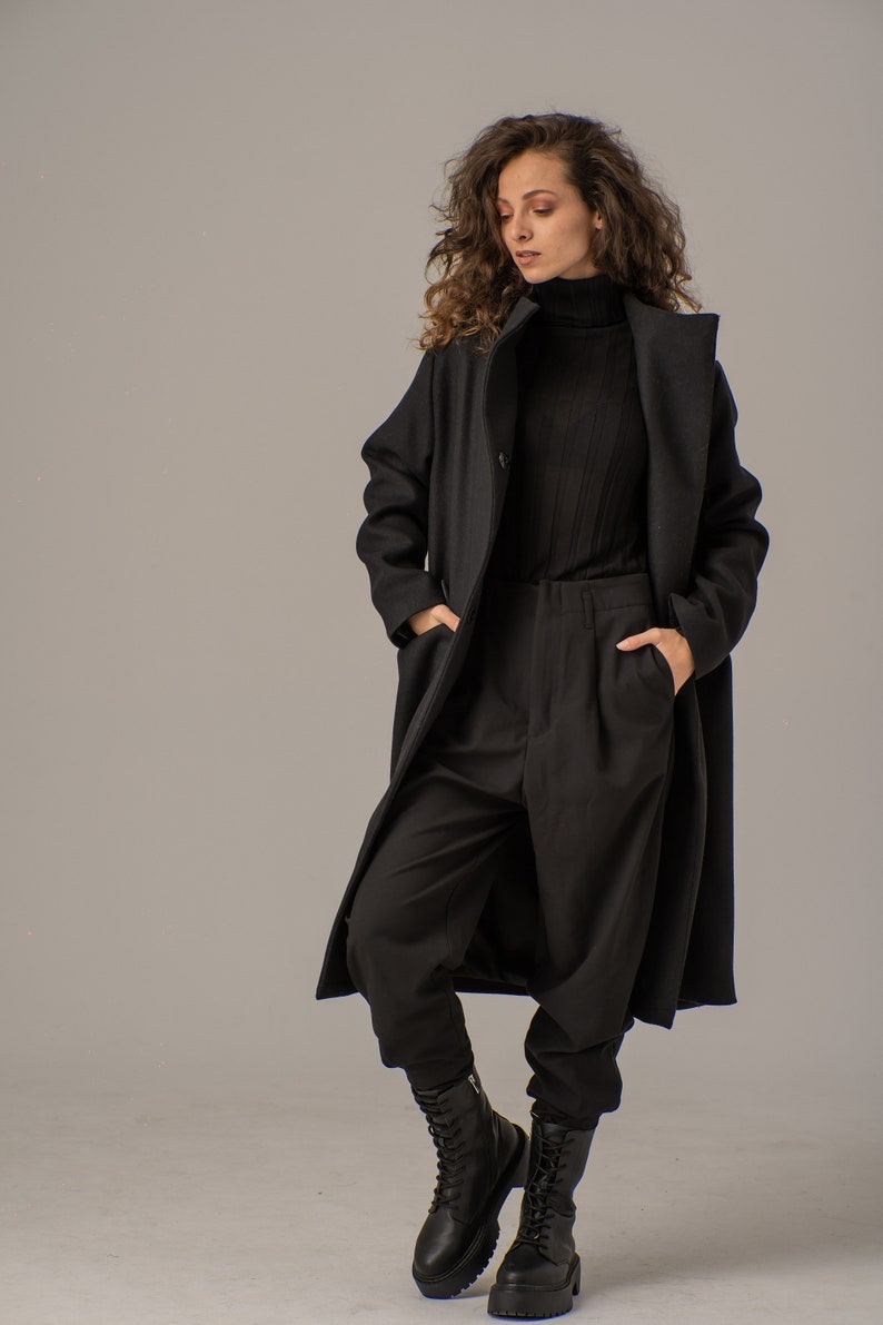 May include: A woman wearing a black long-sleeved turtleneck shirt, black pants, and a black long coat. She is wearing black lace-up boots.