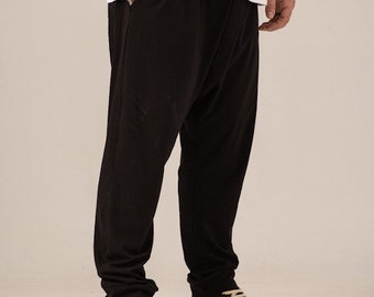 May include: A person wearing black pants with a unique design and a white t-shirt. They are wearing black and cream sneakers.