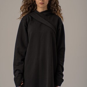 Pode incluir: Uma camisola de capuz preta de manga comprida com um design cruzado na gola. A camisola &eacute; feita de um tecido macio e confort&aacute;vel e tem um caimento descontra&iacute;do.