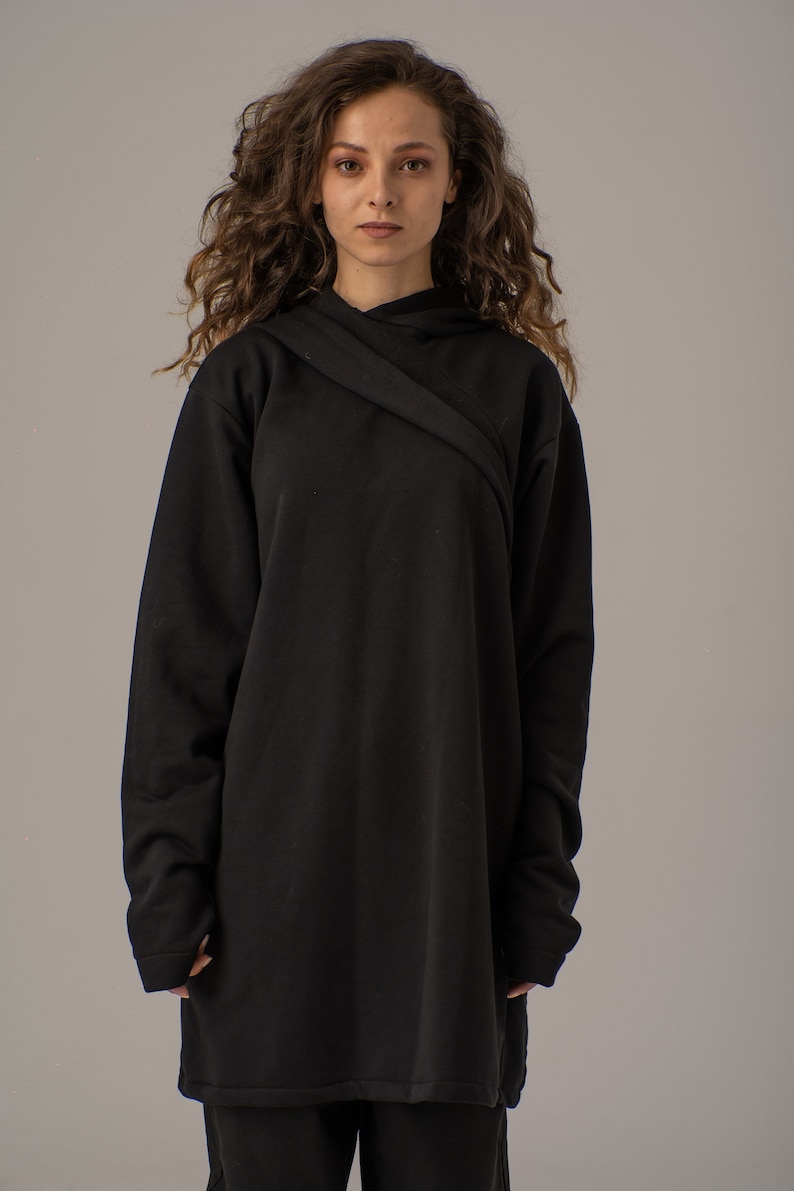 Pode incluir: Uma camisola de capuz preta de manga comprida com um design cruzado na gola. A camisola &eacute; feita de um tecido macio e confort&aacute;vel e tem um caimento descontra&iacute;do.