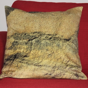 May include: A decorative throw pillow with a stone-like pattern in shades of brown, beige, and green. The pillow is made of a soft, textured fabric and has a subtle sheen.