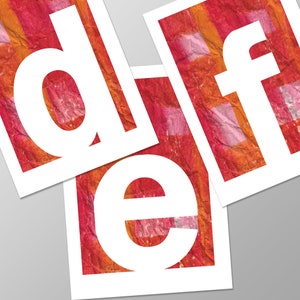 May include: Three white letters, "d", "e", and "f", cut out of paper and placed on a red and orange patterned background.
