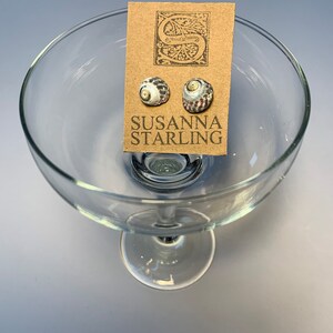 May include: A pair of shell earrings with a white, grey, and brown pattern. The earrings are displayed on a card with the text "SUSANNA STARLING".
