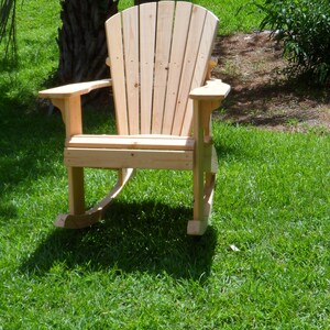 May include: A wooden rocking chair with a high back and wide arms, sitting on a grassy lawn.
