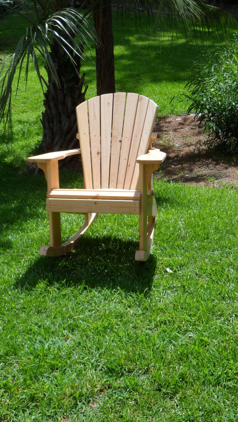 May include: A wooden rocking chair with a high back and wide arms, sitting on a grassy lawn.
