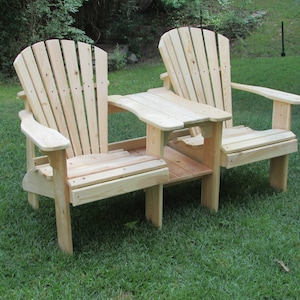 Könnte beinhalten: Zwei Adirondack-Stühle aus Holz mit einem kleinen Tisch dazwischen. Die Stühle sind aus Naturholz gefertigt und haben eine Lattenrücklehne und einen Latten-Sitz. Der Tisch ist ebenfalls aus Naturholz gefertigt und hat eine rechteckige Tischplatte.