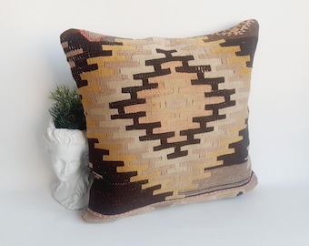 May include: A brown, beige, and yellow patterned throw pillow with a geometric design. The pillow is made of woven fabric and has a fringed edge.