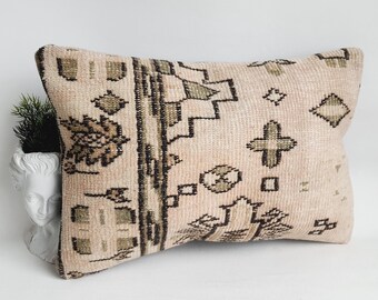 May include: A rectangular pillow with a beige background and a geometric pattern in shades of brown and green. The pillow is made of a soft, woven fabric and has a fringed edge.