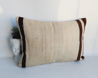May include: A long, rectangular pillow with a white woven fabric and brown stripes along the edges. The pillow is lying on a white surface.