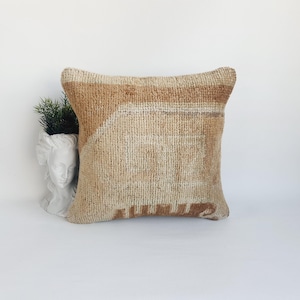 May include: Square beige and brown woven cushion with a geometric design. The cushion has a textured surface and a soft, neutral colour palette. The cushion is a decorative home accent.
