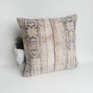 May include: A white and blue patterned throw pillow with a faded, vintage look. The pillow is made of a soft, woven fabric and has a subtle geometric design.