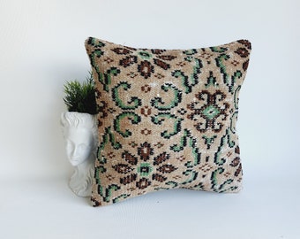 May include: A square throw pillow with a beige background and a green, brown, and black floral pattern.