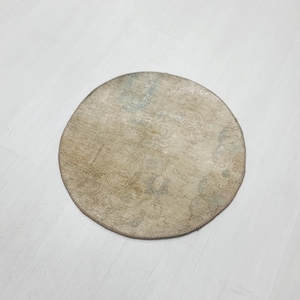 May include: A round, cream-colored rug with a faded floral pattern. The rug has a light blue and brown color scheme.