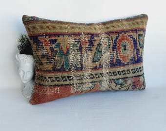 May include: A rectangular pillow with a colorful, patterned design. The pillow is made from a woven fabric with a distressed look. The colors in the pattern include red, blue, green, and brown.