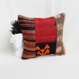 May include: A colorful patchwork pillow with a red, orange, brown, and black geometric pattern. The pillow is made of woven fabric and has a soft, textured surface.