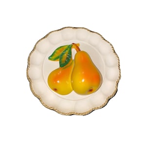 Op de afbeelding: Een decoratieve witte schaal met een geschulpte rand en een touwachtige rand. De schaal toont een paar geel-oranje peren met groene bladeren. De peren zijn het centrale punt van de schaal en voegen een vleugje natuur toe aan het ontwerp.