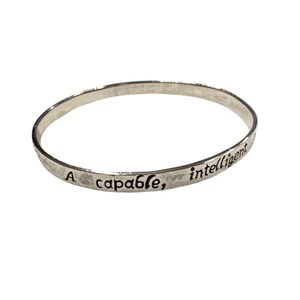 May include: A silver-colored bangle bracelet with the words "A capable, intelligent" engraved on the outside. The bracelet is circular and appears to be made of metal. The text is in a simple, sans-serif font.