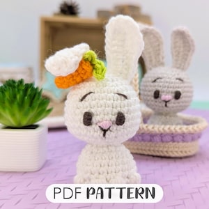 May include: Two crocheted bunny amigurumi toys. One bunny is white with a carrot and green leaves on its head. The other bunny is gray and is sitting in a crocheted basket. The text "PDF PATTERN" is at the bottom of the image.