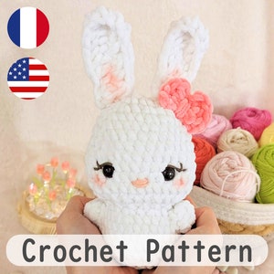 May include: A white crocheted bunny with pink ears and a pink heart-shaped bow. The bunny has black eyes and a pink nose. The bunny is sitting in a basket with colorful yarn balls.