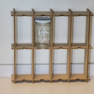 Può includere: Una griglia di cartone con 12 scomparti, uno dei quali contiene un barattolo di vetro trasparente con un coperchio bianco.