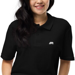 May include: Black polo shirt featuring a white embroidered rhinoceros emblem on the chest. The shirt has short sleeves and a collared neckline. The material looks soft and comfortable.