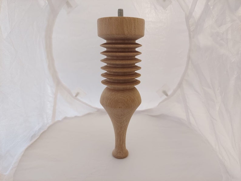 May include: A light-colored wooden furniture leg with a threaded top and a decorative, ribbed design. The leg has a turned, bulbous shape and a tapered foot. The overall design is classic and elegant.