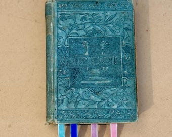 May include: Four colorful ribbon bookmarks with silver bear charms. The bookmarks are attached to an old, green book with ornate designs.