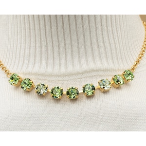 May include: A gold chain necklace with a row of light green and dark green round crystals.