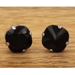 May include: A pair of stud earrings featuring square-cut black faceted stones. Each stone is secured in a silver-toned metal setting with four prongs at the corners, creating a clean and symmetrical appearance for these small, dark jewelry pieces.