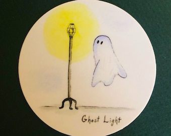 Puede incluir: Un fantasma blanco con dos ojos negros se encuentra junto a una farola negra con una luz amarilla. El texto "Ghost Light" está escrito debajo de la imagen.