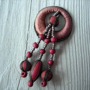 May include: A pink and brown fabric circle with a beaded tassel. The tassel is made of red and silver beads.