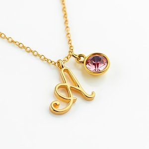May include: A gold necklace with a cursive letter A charm and a pink crystal pendant.