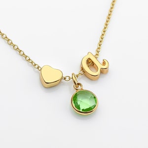 May include: Gold necklace with a heart charm, a letter 'a' charm, and a green gemstone pendant.