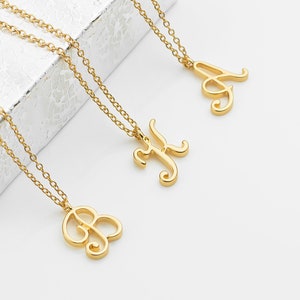May include: Three gold necklaces with cursive letter pendants. The necklaces are on a white surface.