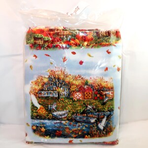 May include: A rectangular fabric panel encased in clear plastic packaging, featuring a printed autumn landscape scene with a house, trees with orange and yellow foliage, a river, small boats, and falling leaves against a light blue sky background.