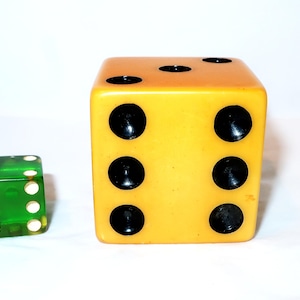 May include: Two dice are shown against a white background. One die is a large, yellow cube with black dots. The other die is a smaller, transparent green cube with white dots. The dice are used for games.