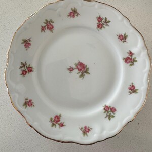 Puede incluir: Plato de porcelana blanca con borde festoneado y ribete dorado. El plato está decorado con pequeños racimos de rosas rosas y hojas verdes. Un diseño delicado y elegante para servir alimentos.