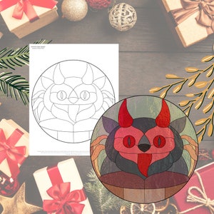 May include: A stained glass design featuring a cartoon devil with red horns, eyes, and tongue. The design is circular and includes a black and gray color scheme. A black and white line drawing of the same design is also shown.