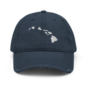 May include: A navy blue distressed baseball cap with a white embroidered outline of the Hawaiian islands.