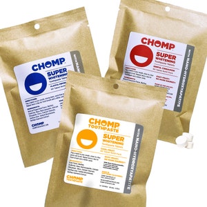 May include: Three brown paper pouches of CHOMP Super Whitening Toothpaste Tablets. Each pouch has a white label with the CHOMP logo and flavor details: Playful Peppermint, Sinful Cinnamon, and Cool Fruit. The tablets are shown in a small pile.