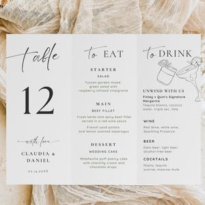 Op de afbeelding: Een witte trouwmenukaart met zwarte tekst. De kaart is verdeeld in drie secties: "Tafel 12", "Om te eten" en "Om te drinken". Het menu bevat voorgerechten, hoofdgerechten, desserts, wijn, bier en cocktails. De kaart is ondertekend met "Claudia & Daniel".