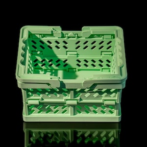 May include: A light green plastic folding storage crate with a grid pattern. The crate is empty and sitting on a black surface.