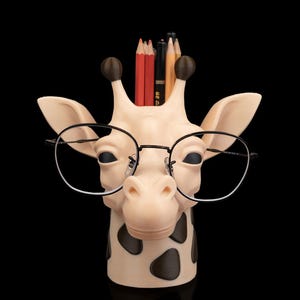 May include: A whimsical giraffe-shaped pencil holder with black-rimmed glasses. The holder is beige with brown spots and holds several pencils. The background is black.