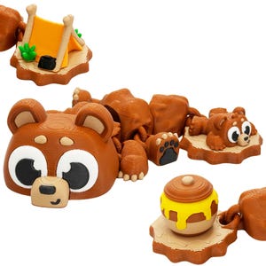 May include: A brown bear-themed toy set featuring a tent, honey pot, and bear cub. The bear has large eyes and a small nose. The tent is orange with brown poles. The honey pot is brown with yellow honey. The cub is lying down.