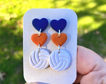 May include: A pair of earrings with a volleyball charm, orange heart charm, and blue heart charm.