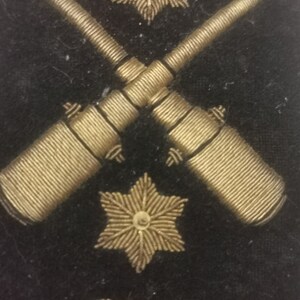 May include: A black fabric patch with gold embroidered details. The patch features two crossed cannons, two gold stars, and the letters "CA".